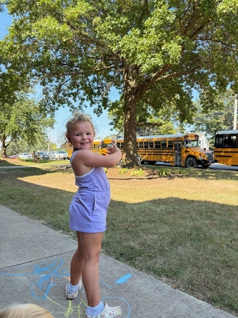 child care student waving at school buses outside middle school