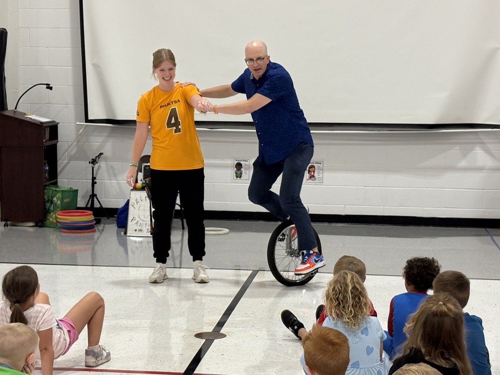Man riding unicycle with assistance of staff member