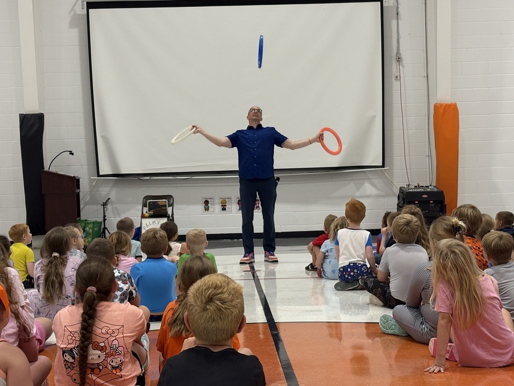 Man juggling hoops while students watch during assembly