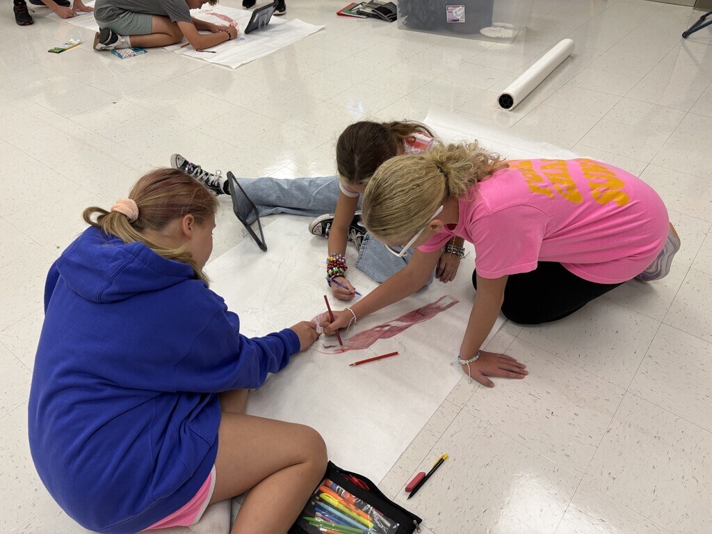 students drawing the skeletal and muscular system on large sheets of paper