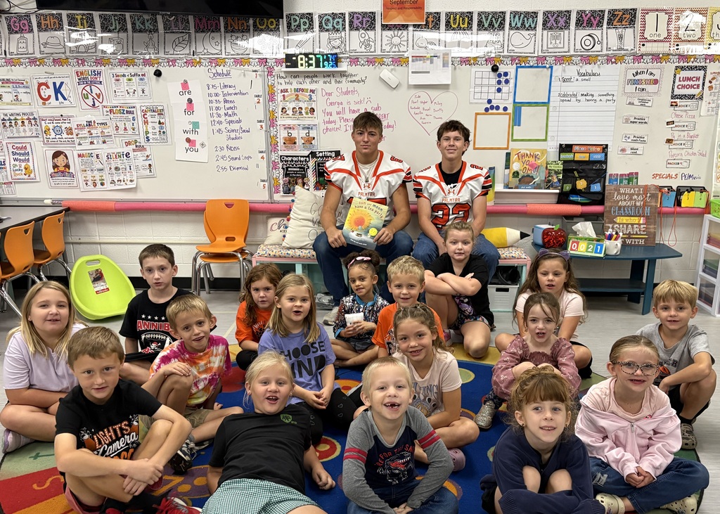 students listening to football players read a book and posing for picture