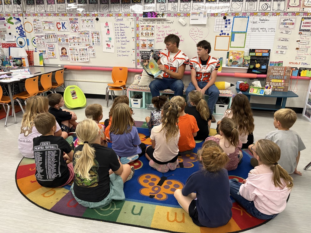 students listening to football players read a book and posing for picture
