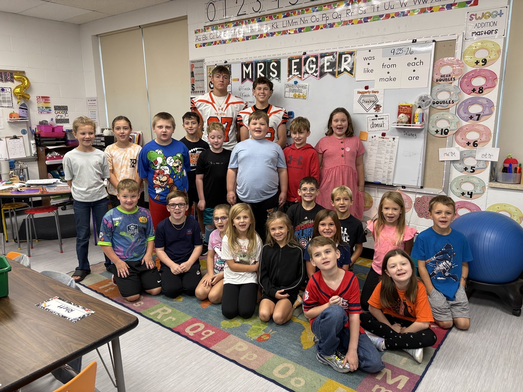 students listening to football players read a book and posing for picture