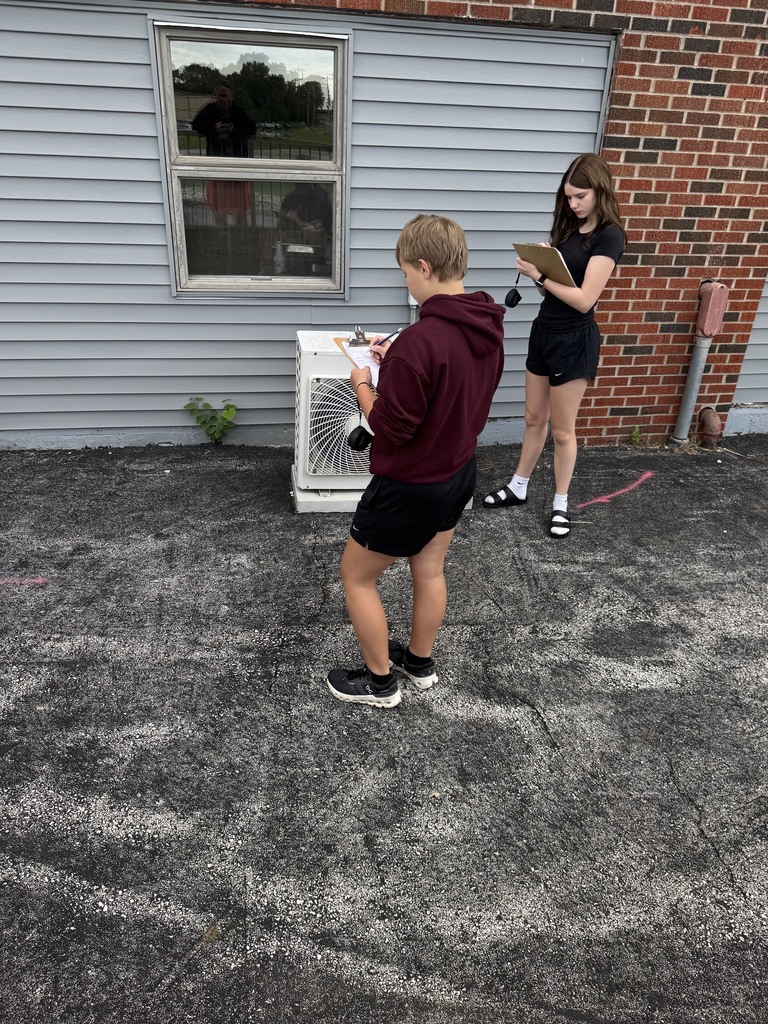 2 students with clipboards studying geometry shapes outside middle school