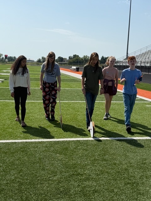 students using hodometers they made in class to measure distance on football field