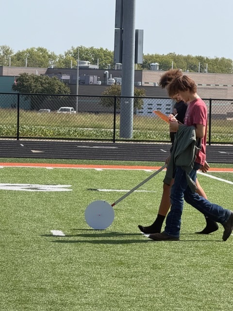 students using hodometers they made in class to measure distance on football field