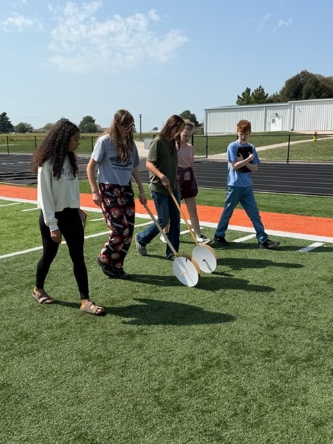 students using hodometers they made in class to measure distance on football field