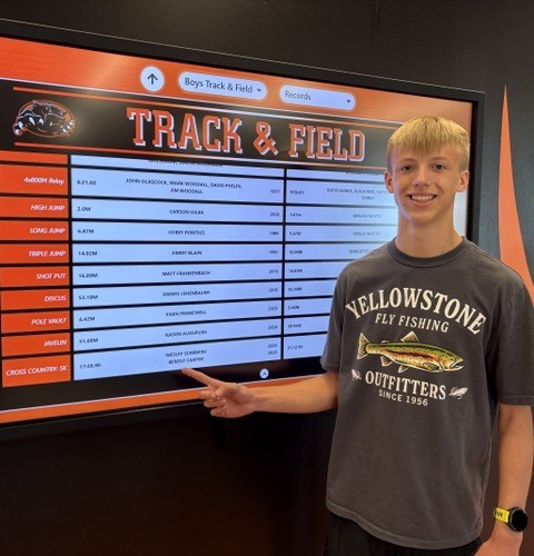 student standing by record board with his new XC record of 17:39:90