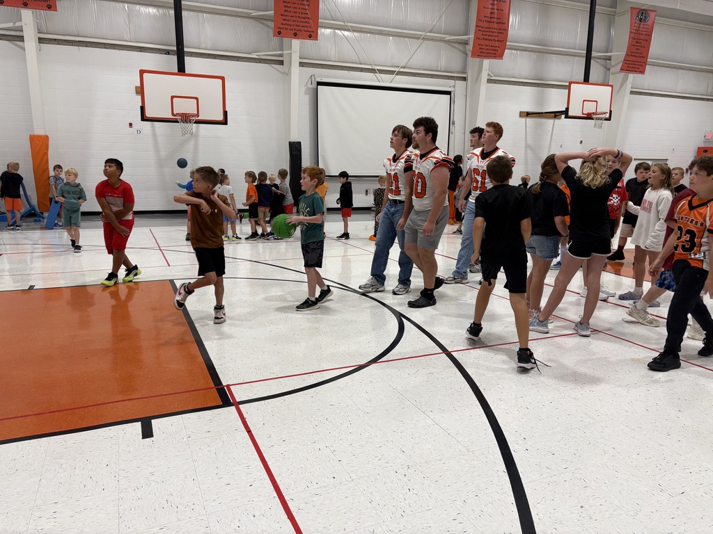 football player playing basketball with elementary students