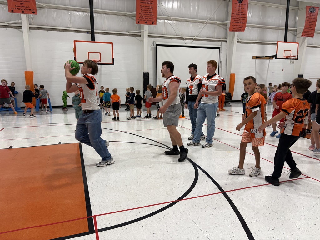 football players playing basketball with elementary students