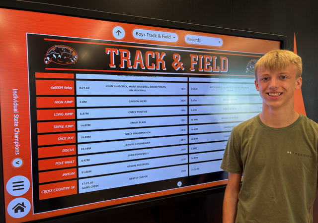 student standing in front of track & field record board with new XC record