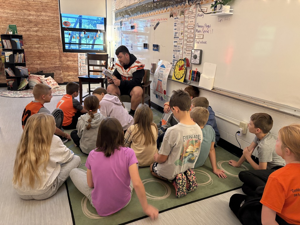 football player reading to 3rd grade students