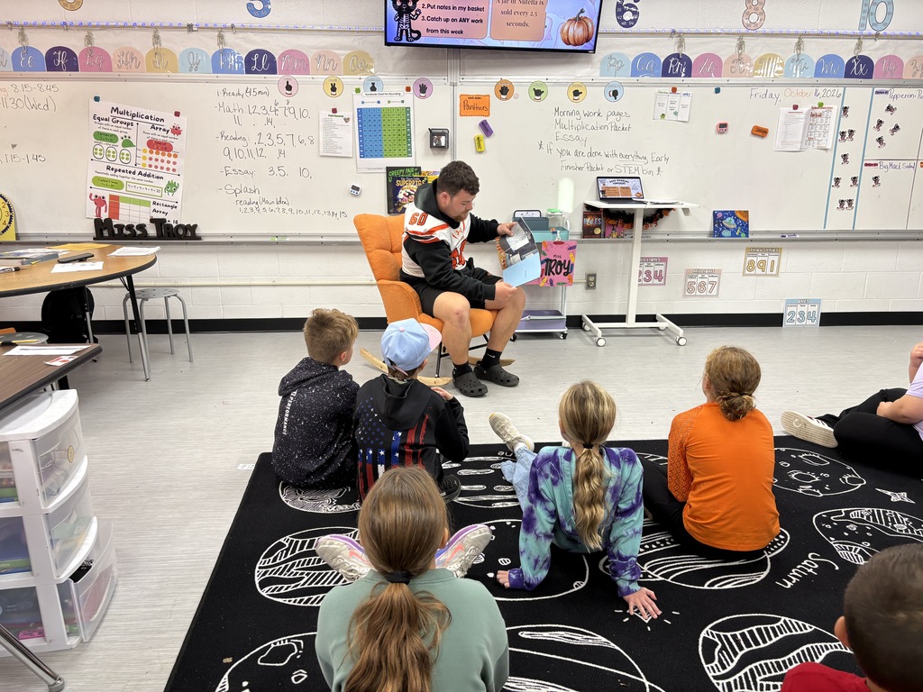 football player reading to 3rd grade students