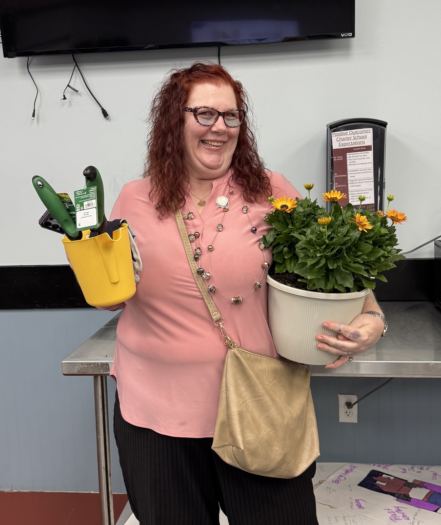 Person in pink shirt holds gardening tools in one hand and a potted plant in the other.