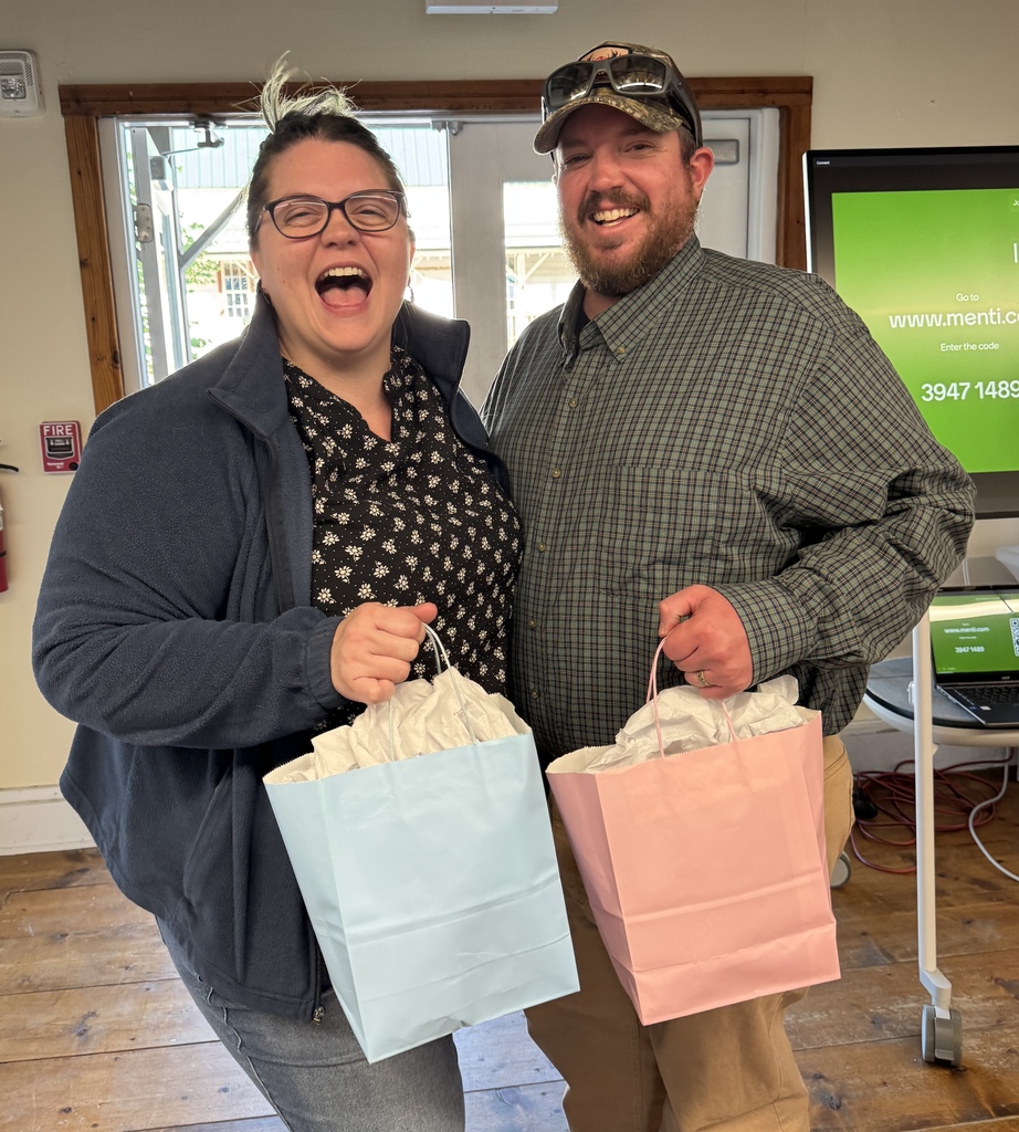 A man and woman smiling and holding gift bags, standing in a room with wooden flooring.