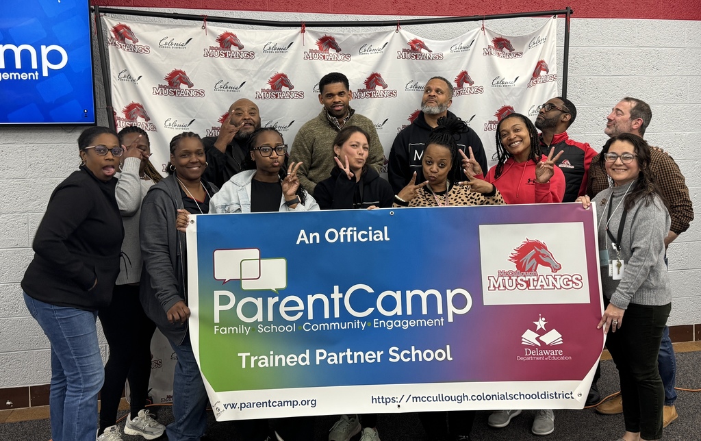 A group of adults posing in front of a large blue and white banner with ParentCamp logo and text.