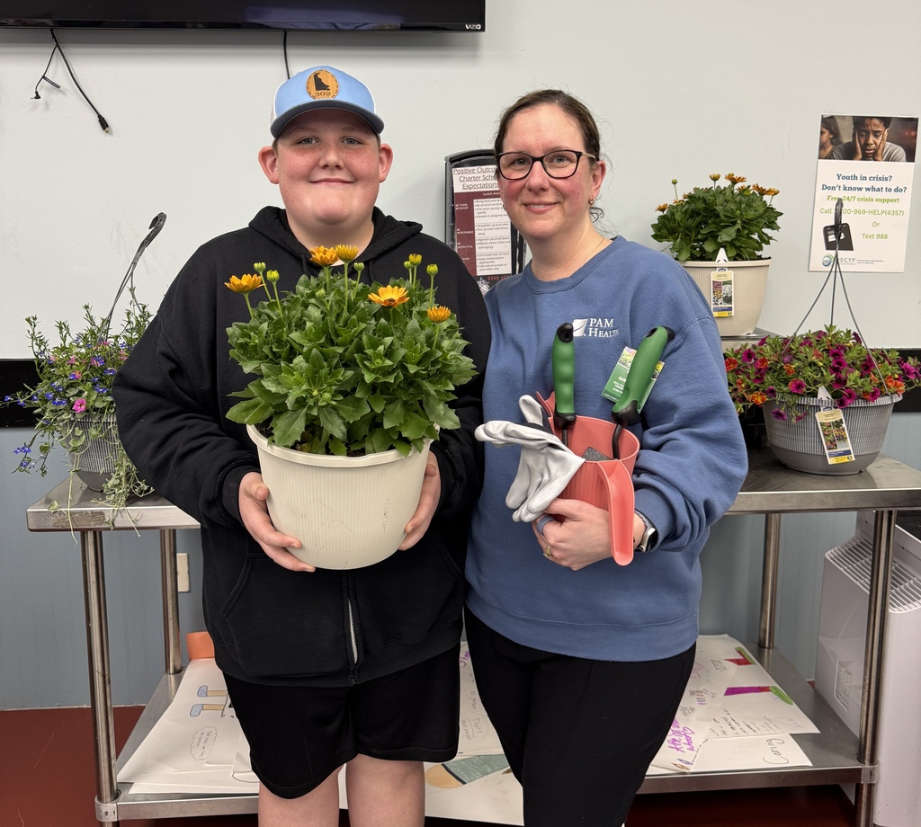 Two people, a man and a woman, stand near a table with potted plants, smiling for a photo.
