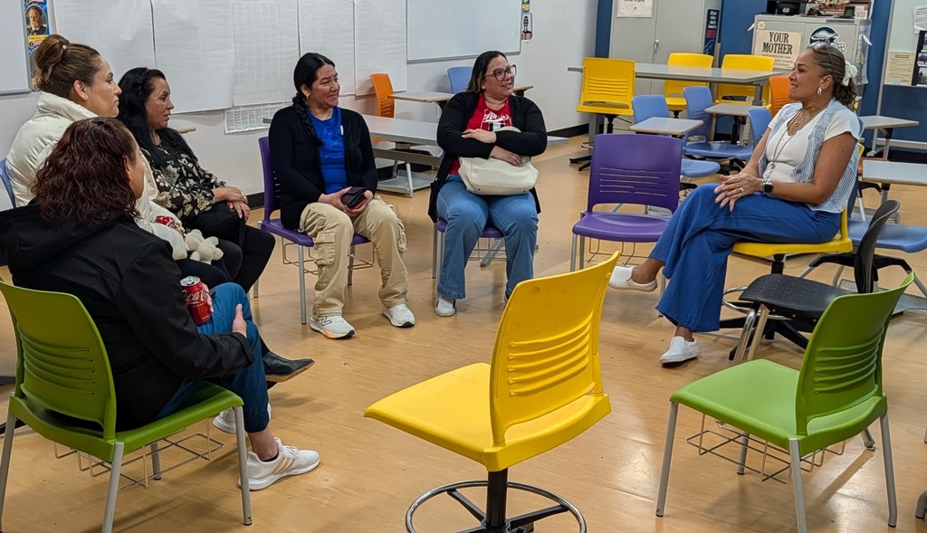 Group of people sitting in colored chairs in a classroom. Some chairs are swiveling.
