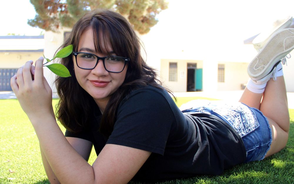 Macayla smiling big, holding a leaf near her face
