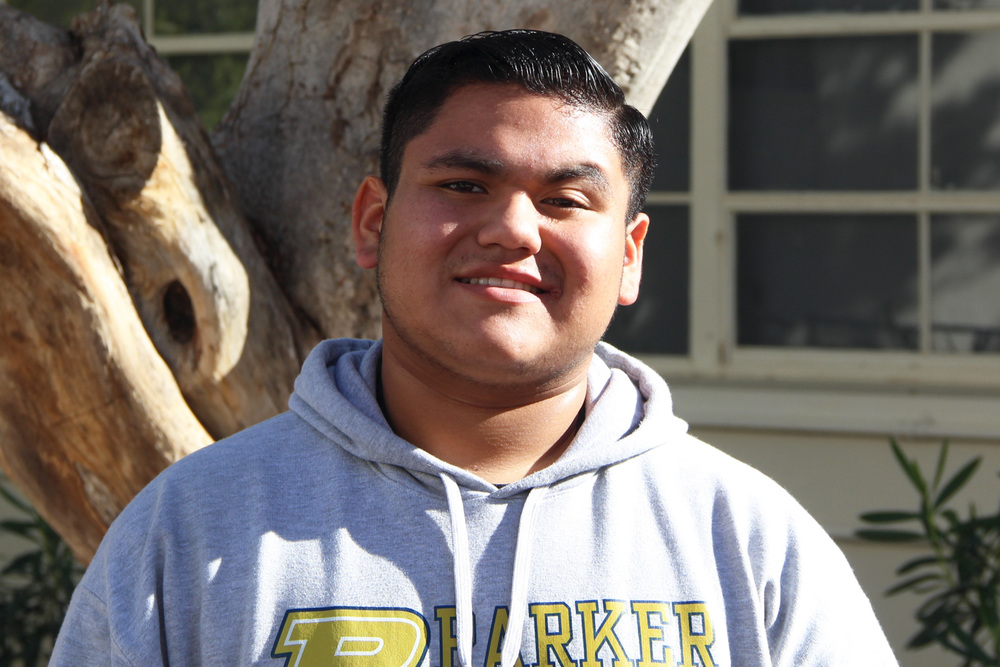 Omar in a Parker High hoodie smiling in the sunshine near a tree
