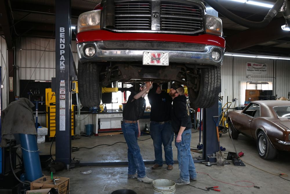 Mr. Keene and two students check under a truck up on a lift.