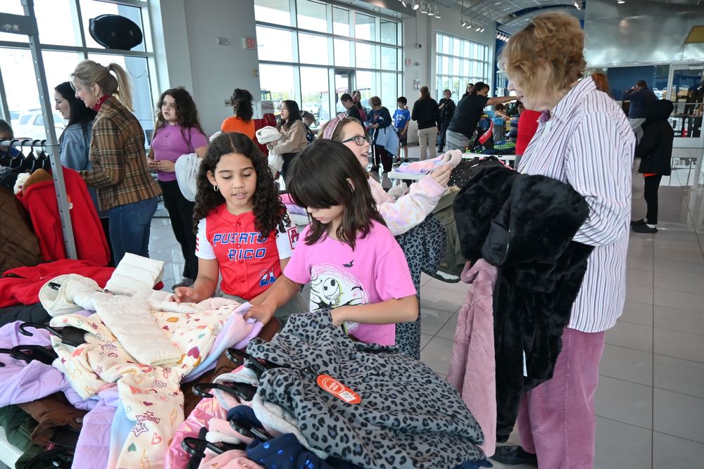 Two girls look for jackets while another shows her choice to a volunteer.