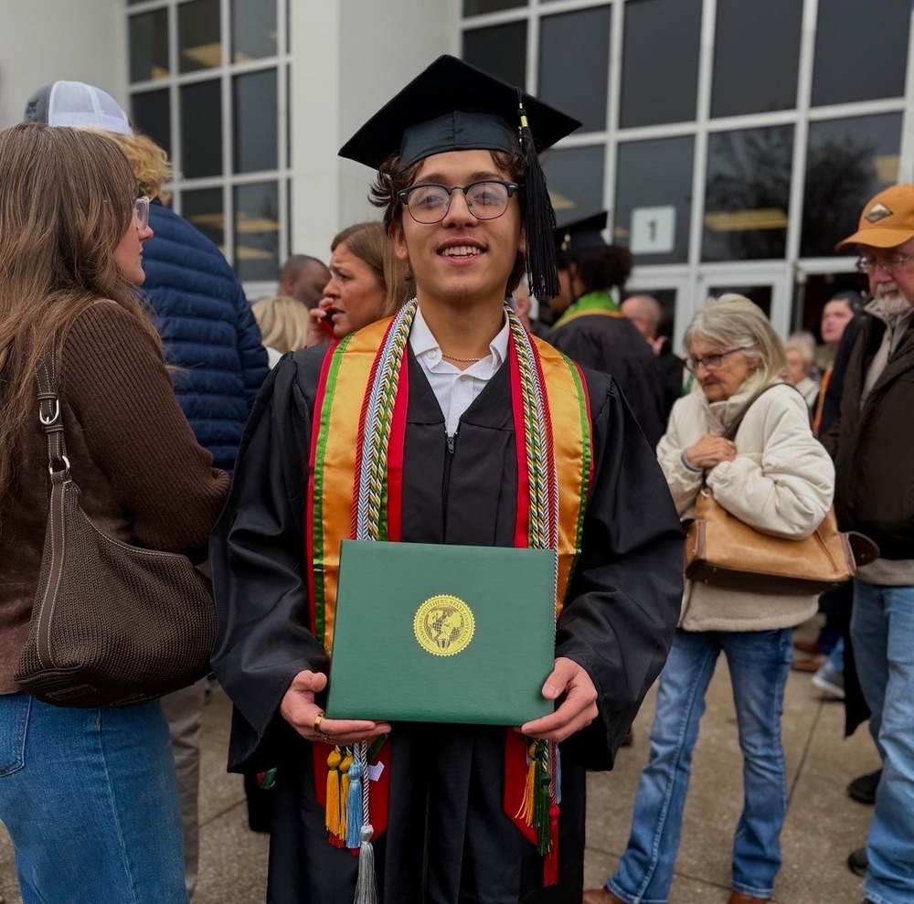 Axl Ramirez, dressed in college grad regalia, stands with his bachlor's degree amid a crowd.