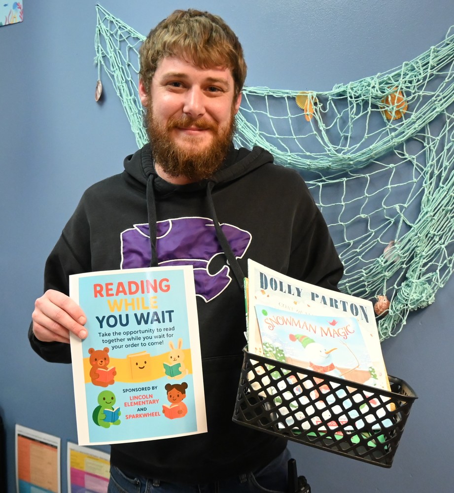 Tanner Smith holds up a sign and basket used for the Reading While You Wait project.