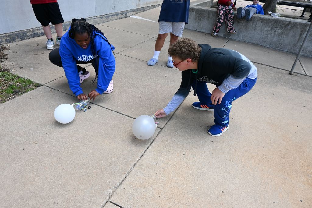 A boy and girl prepare to race their ballon cars.