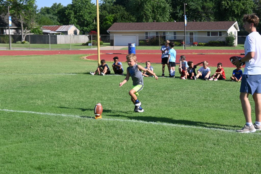 A boy  runs up to kick the football sitting on a holder.