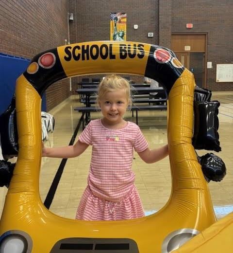 A little girl smiles as she gets her picture taken at the bus transportation table.