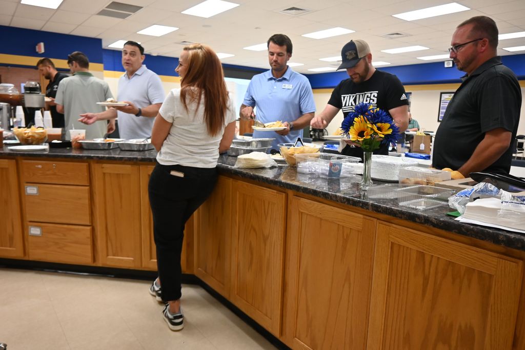 Administrators and teachers get plates of food and chat.