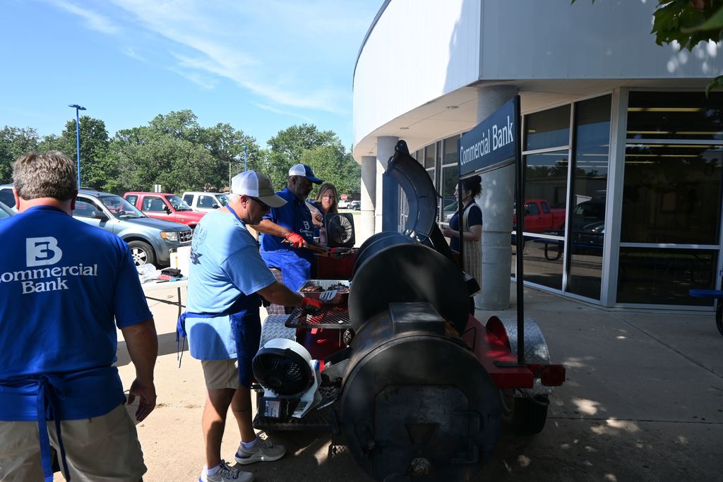 Commercial Bank employees cook burgers on a grill.
