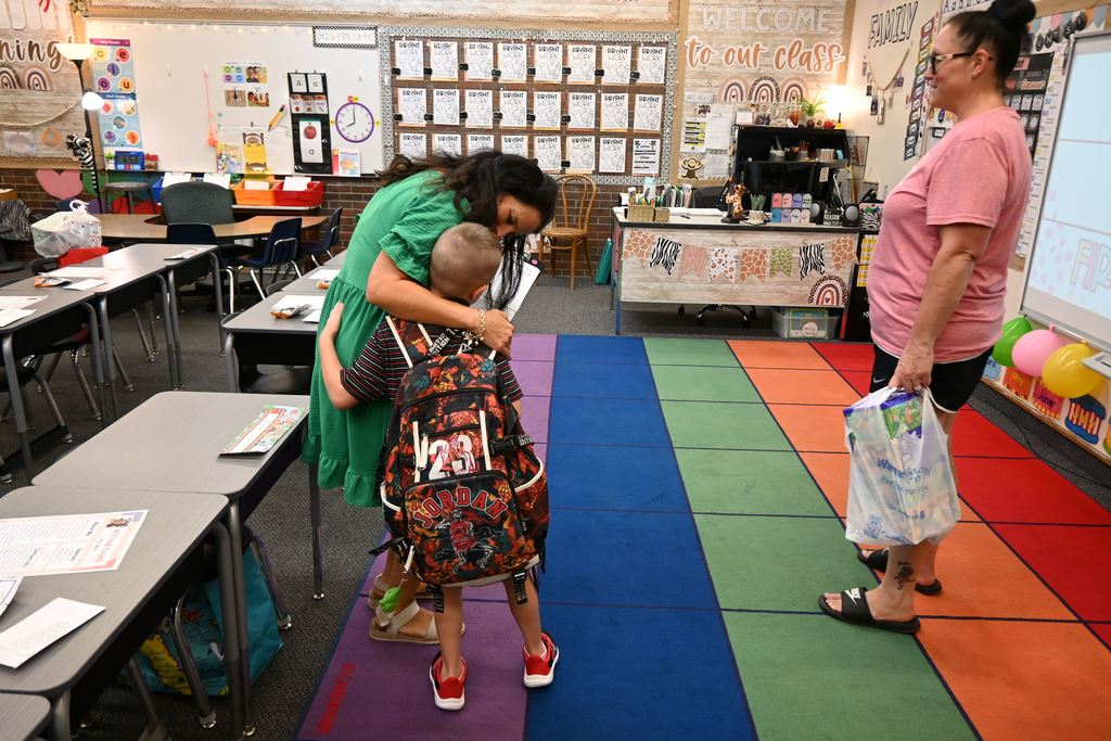 a little boy hugs his teacher as the boys mo  looks on.