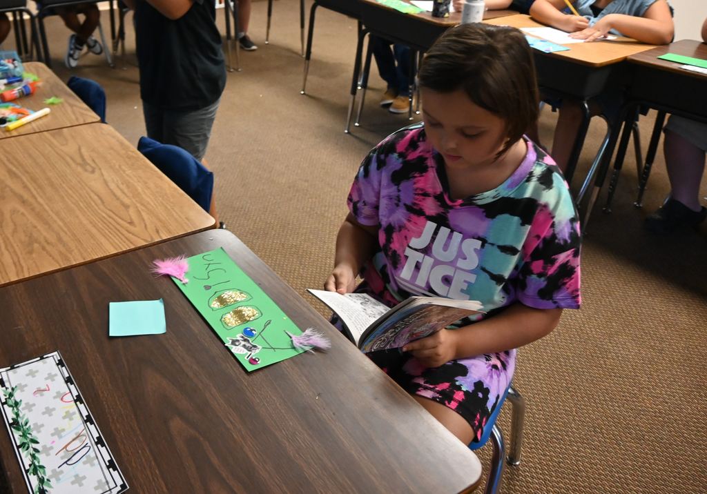 A girl reads a book after finishing her name plate.