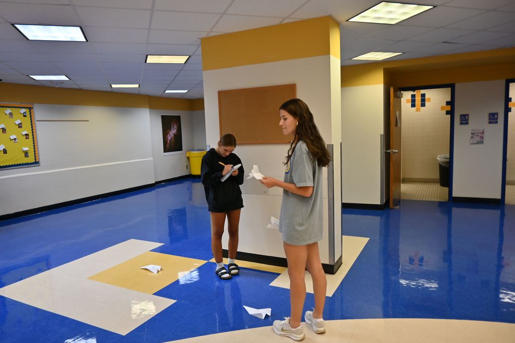 A team mate records results of one of the latest tests  and their paper airplanes lie about them on the floor.