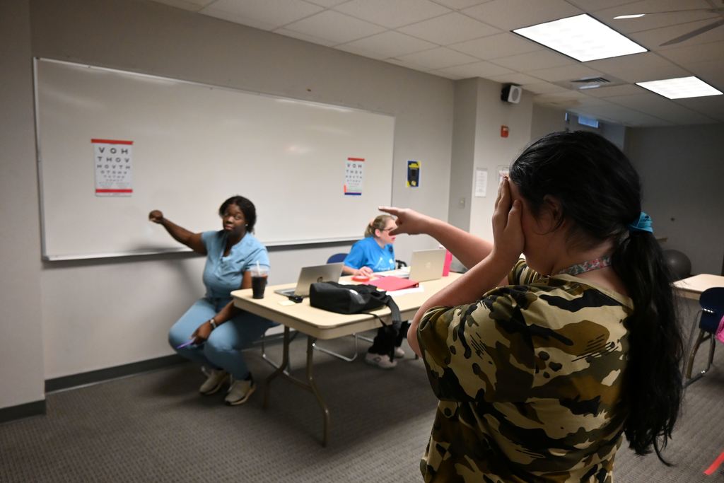 A student covers one eye and reads a line on an eye chart.