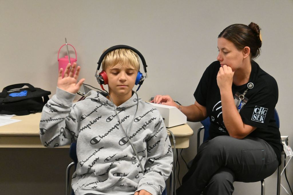 A boy raises his hand on the side he hears a sound produced in the headphones he is wearing.