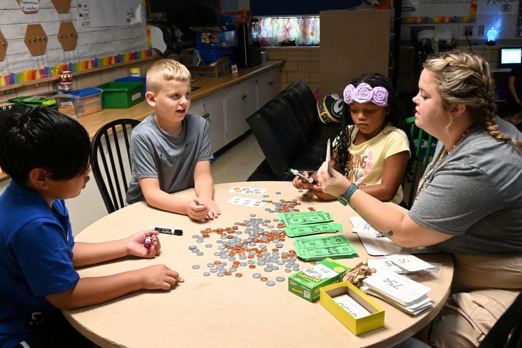 Students count out play money to make correct amounts.