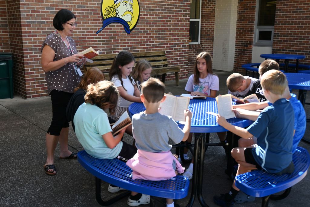 Students sit outside at a picnic table to read.