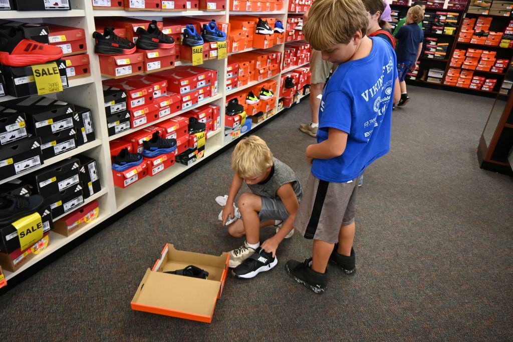 A boy holds a show he likes up to his tennis shoe to see if he thinks it is close to the right size.