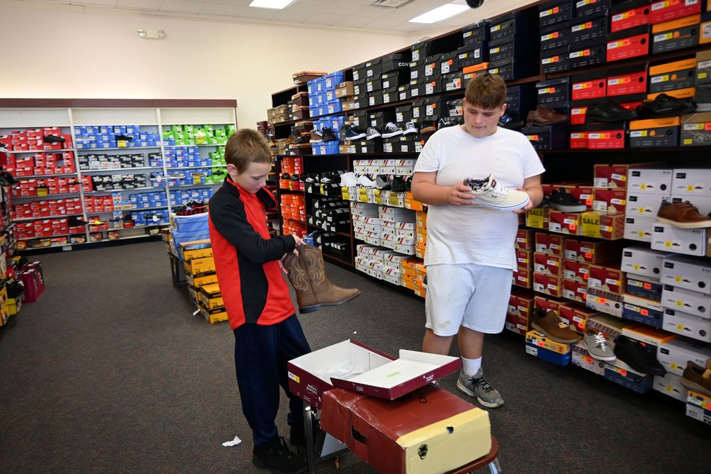 One boy checks out a pir of cowboy boots while another checks out a new pair of tennis shoes.