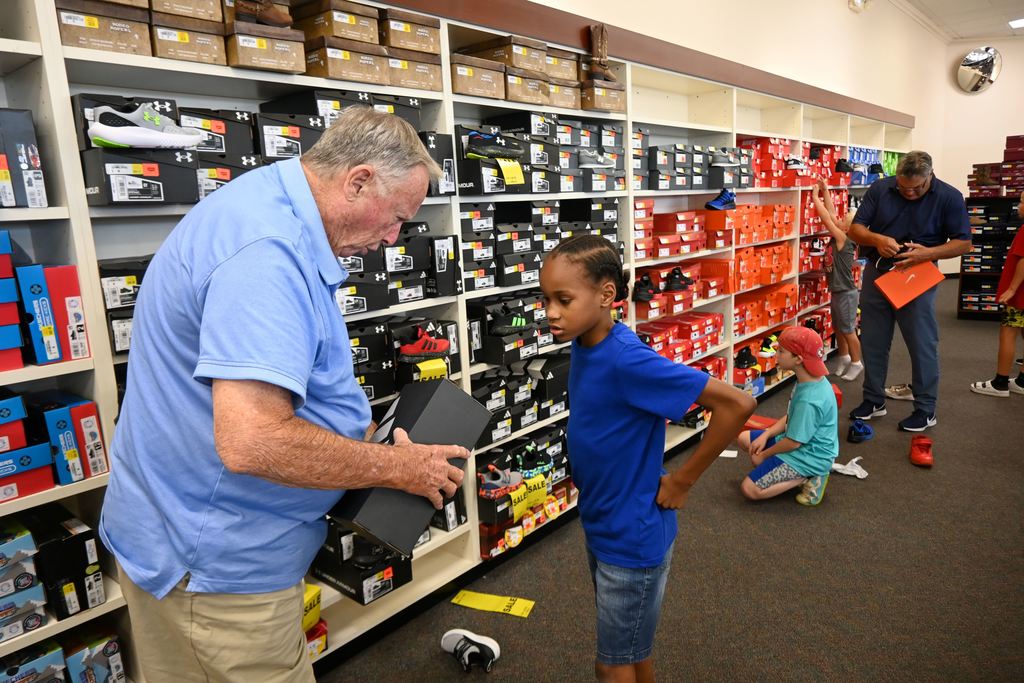 A gentlemena with the church helps a student with checking out the right size of shoe.