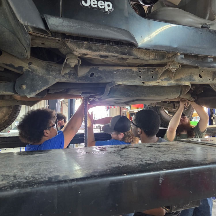 students work under a jeep raised up on a lift.