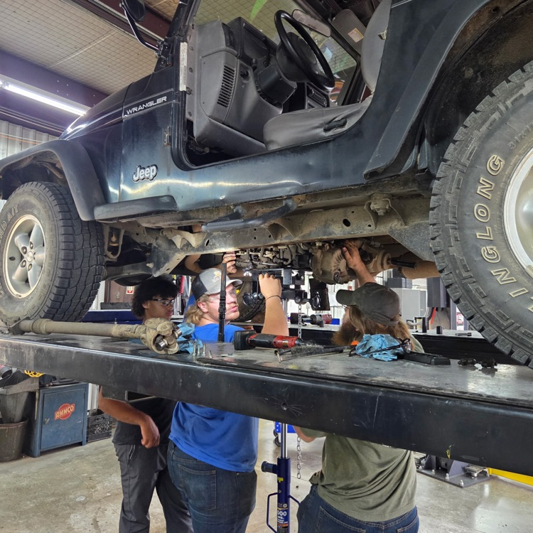 Students work under a jeep raised up on a lift.
