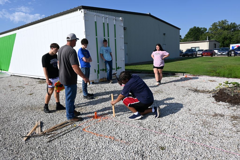 A student drives stakes into the ground to mark corners.