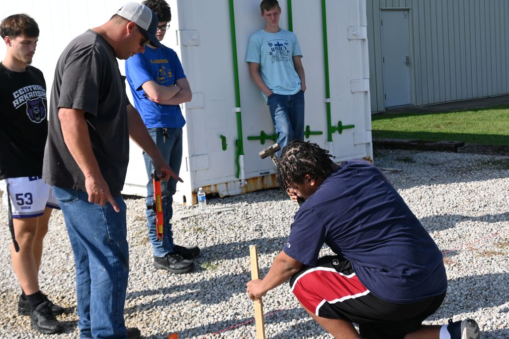 A student drives stakes into the ground to mark corners.