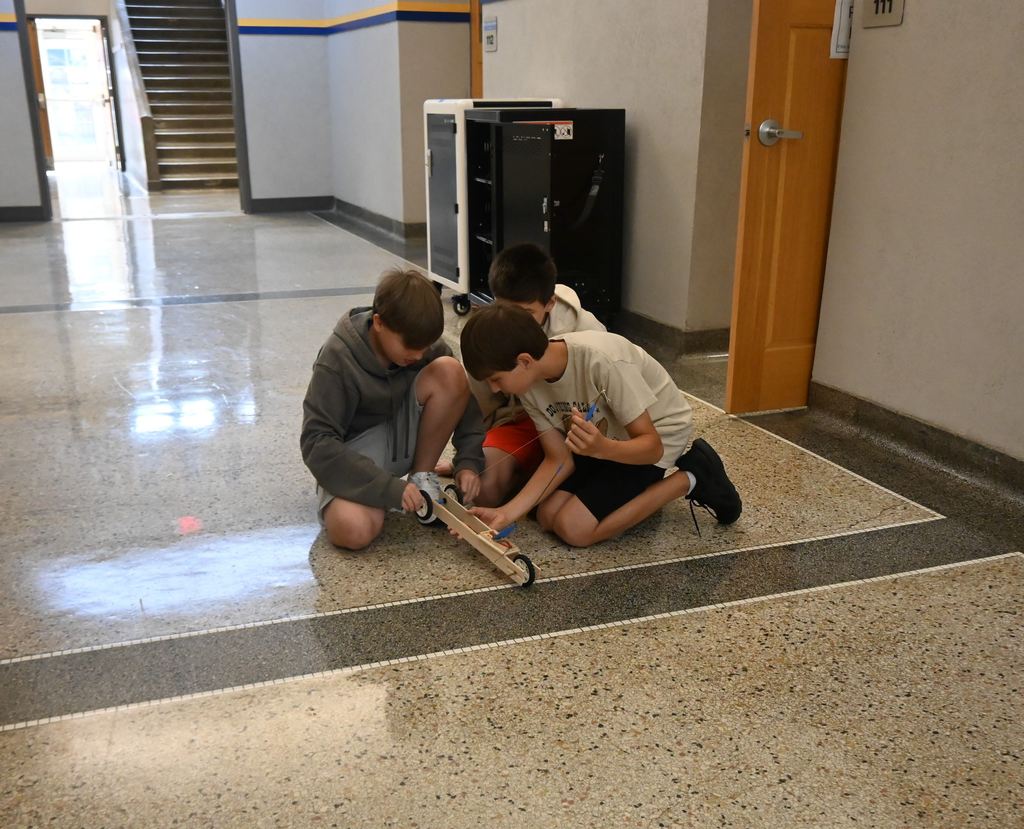Three boys wind up their car to prepare it to race.