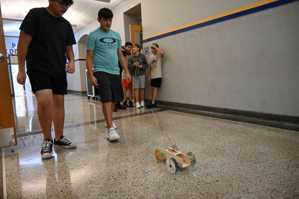 To boys race their car down the hall to get the best distance.