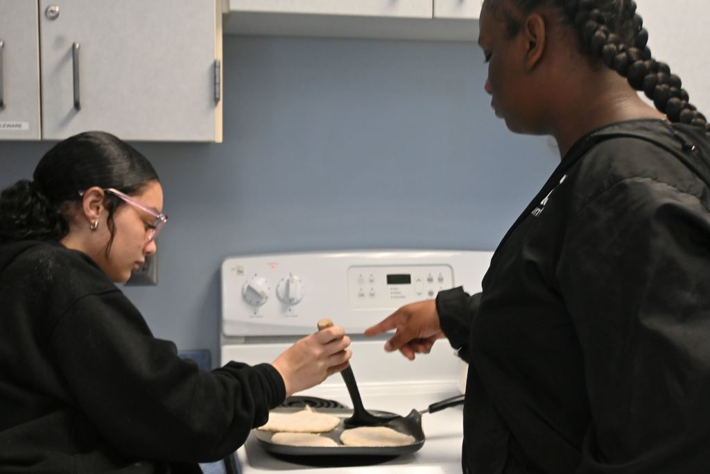 Two girls cook their pita on a griddle.